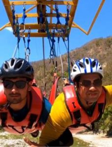 Two men harnessed for adventure sports in rishikesh above a river and mountain landscape